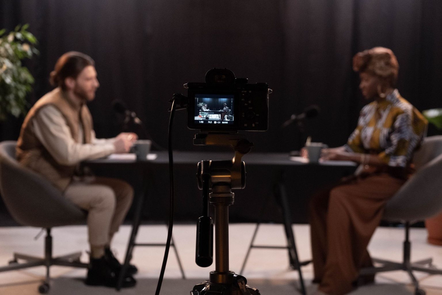 Dois apresentadores gravam um podcast em vídeo em um estúdio equipado com microfones e câmeras.