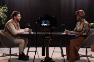 Dois apresentadores gravam um podcast em vídeo em um estúdio equipado com microfones e câmeras.