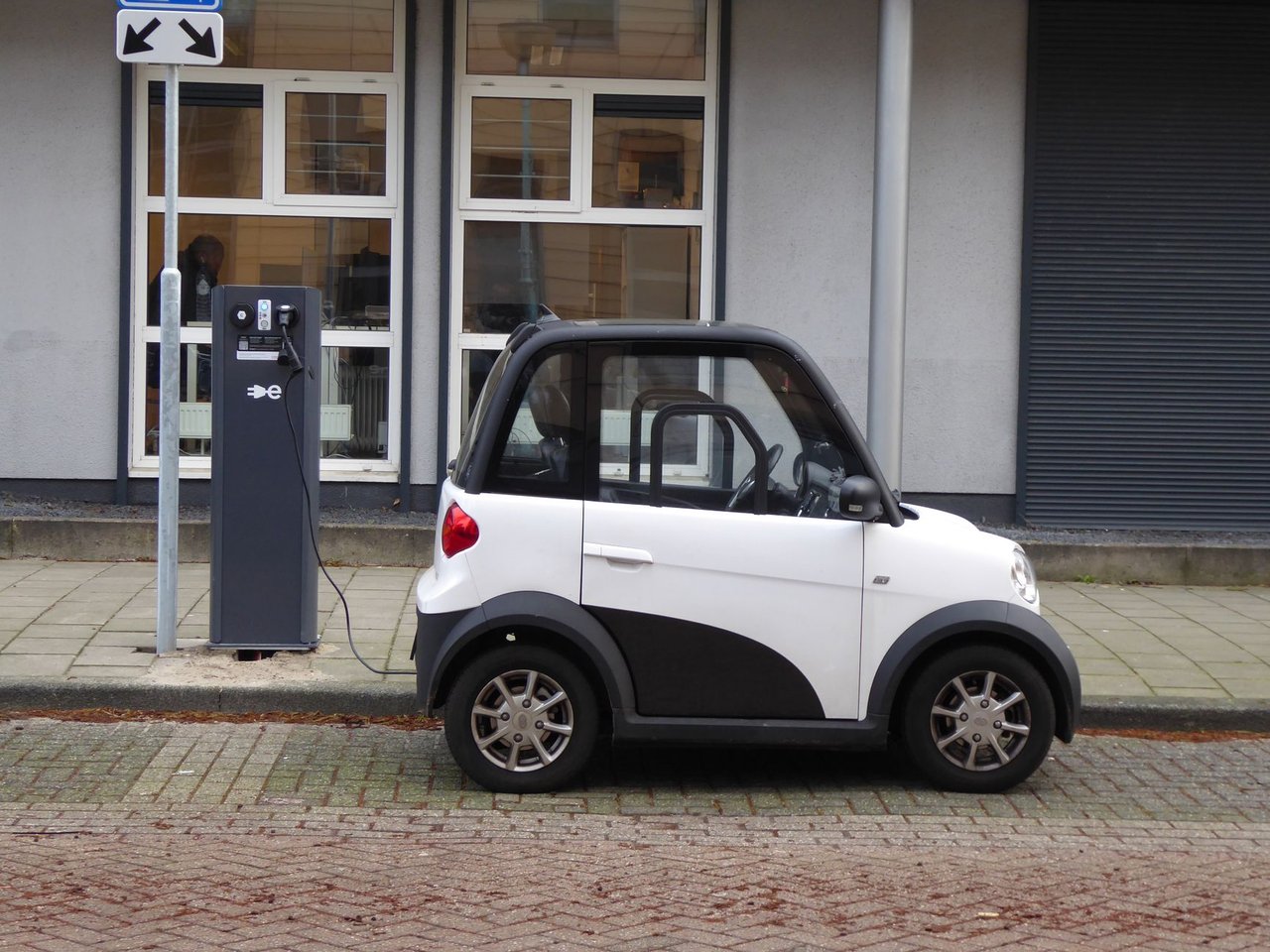 Carro elétrico compacto branco e preto conectado a uma estação pública de recarga.