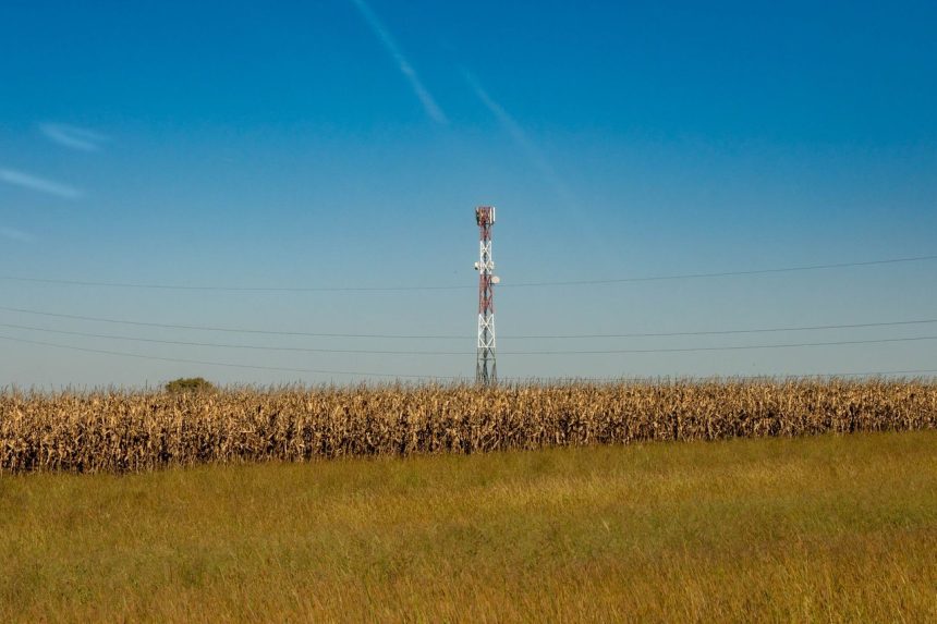 Torre de comunicação instalada em um campo rural sob céu azul.