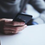 Mão de uma pessoa segurando um smartphone, em contexto de consulta digital a benefício social.